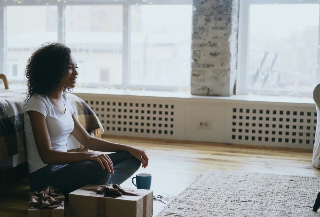 A woman sitting by a window with a warm drink, taking a quiet moment